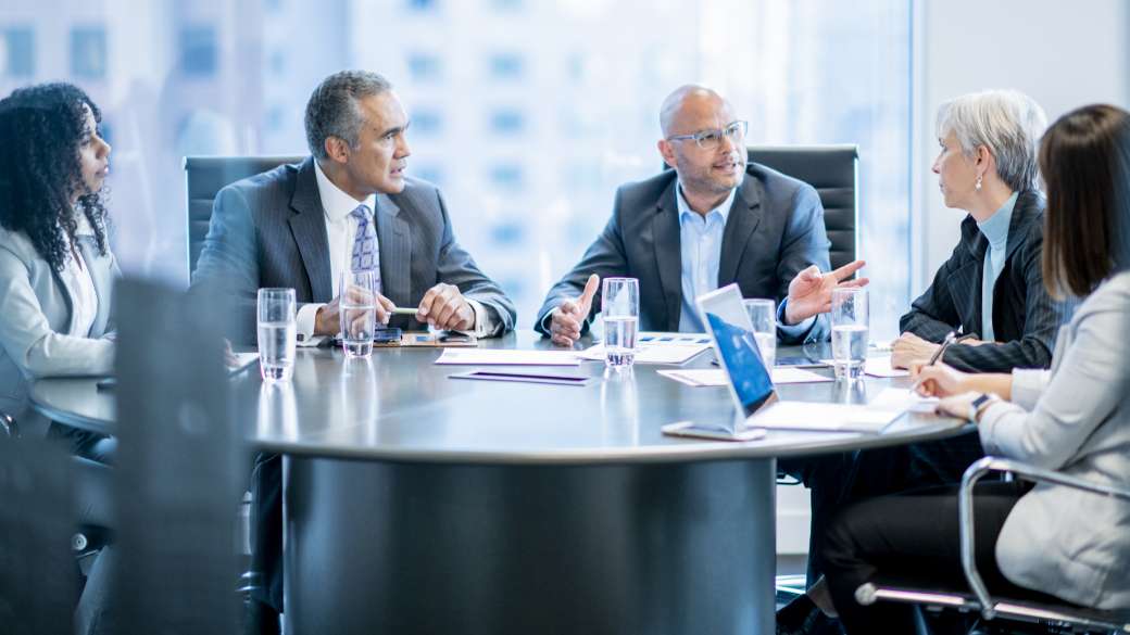 Business people sitting around a table involved in a meeting with various papers and laptop computers on the table