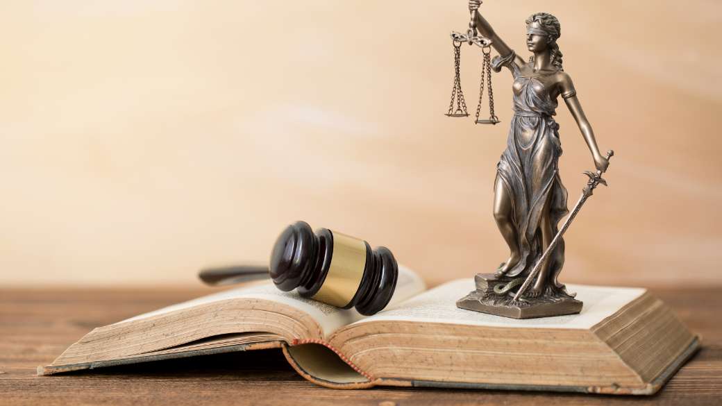 Lady justice statuette alongside a gavel placed on an old book
